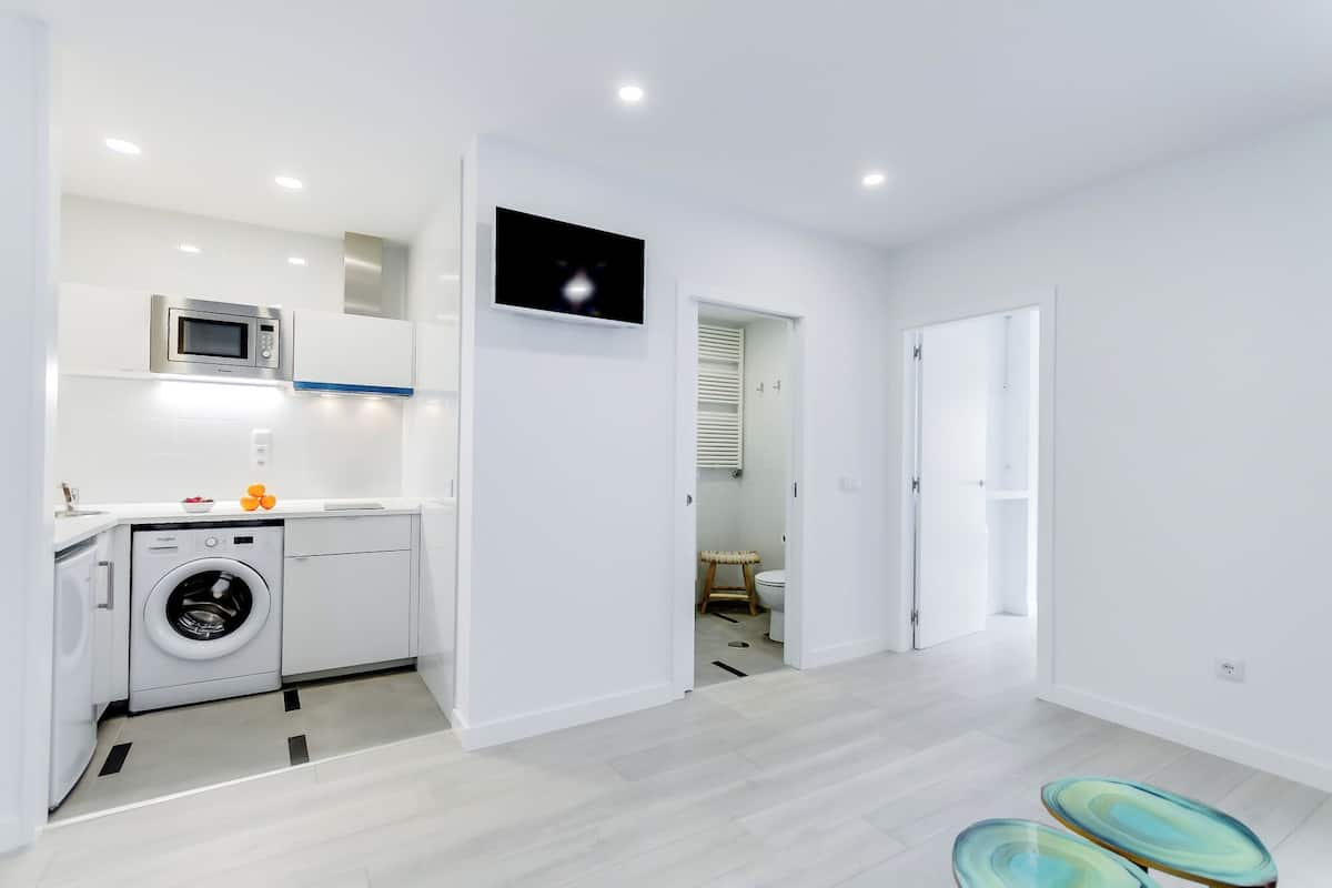 A modern kitchen with a washing machine, microwave, and a flat-screen TV.