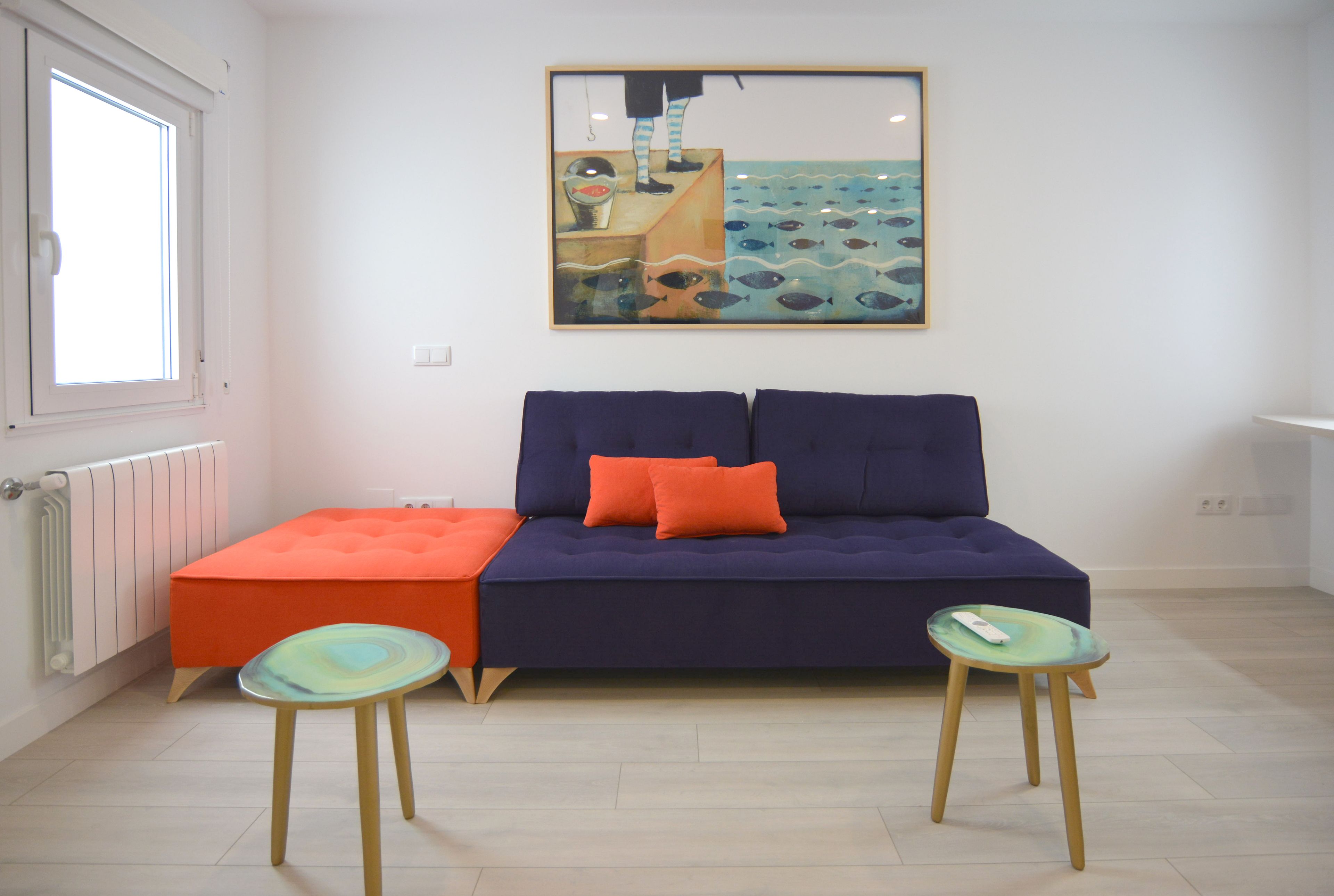 Een moderne woonkamer met een bank, twee krukken, een radiator en een raam.