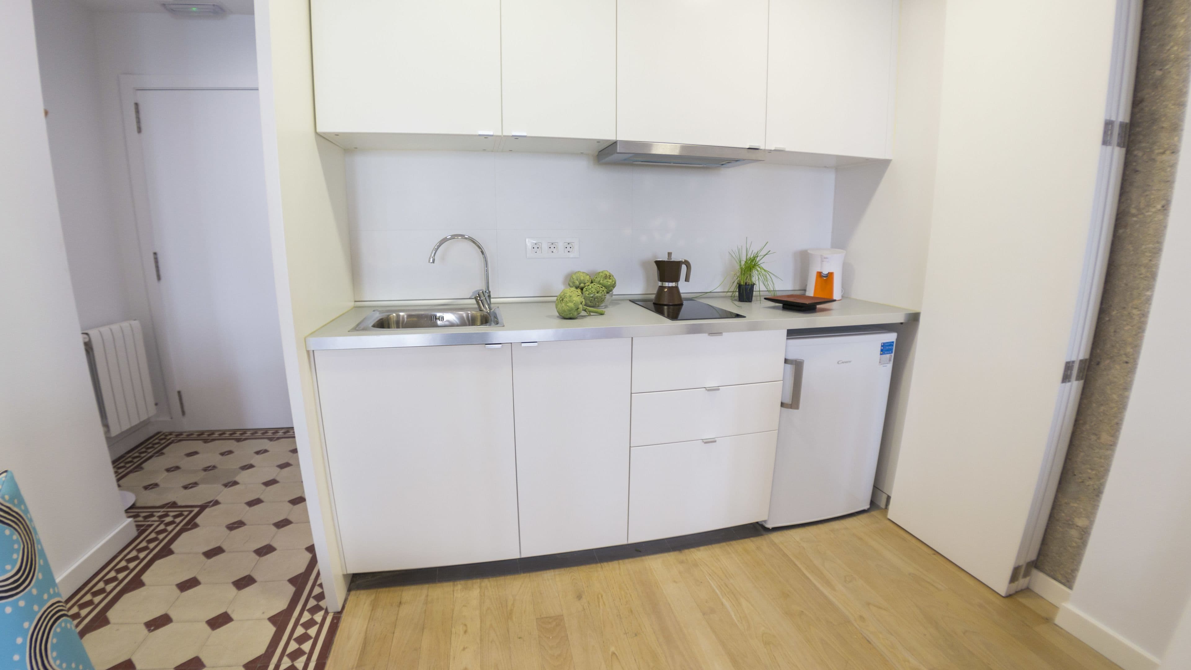 Una cocina compacta con armarios blancos, un lavamanos de acero inoxidable y una cafetera.
