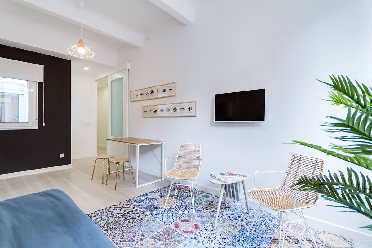 A modern living room with a sofa, a coffee table, two chairs, a TV, and framed artwork on the wall.