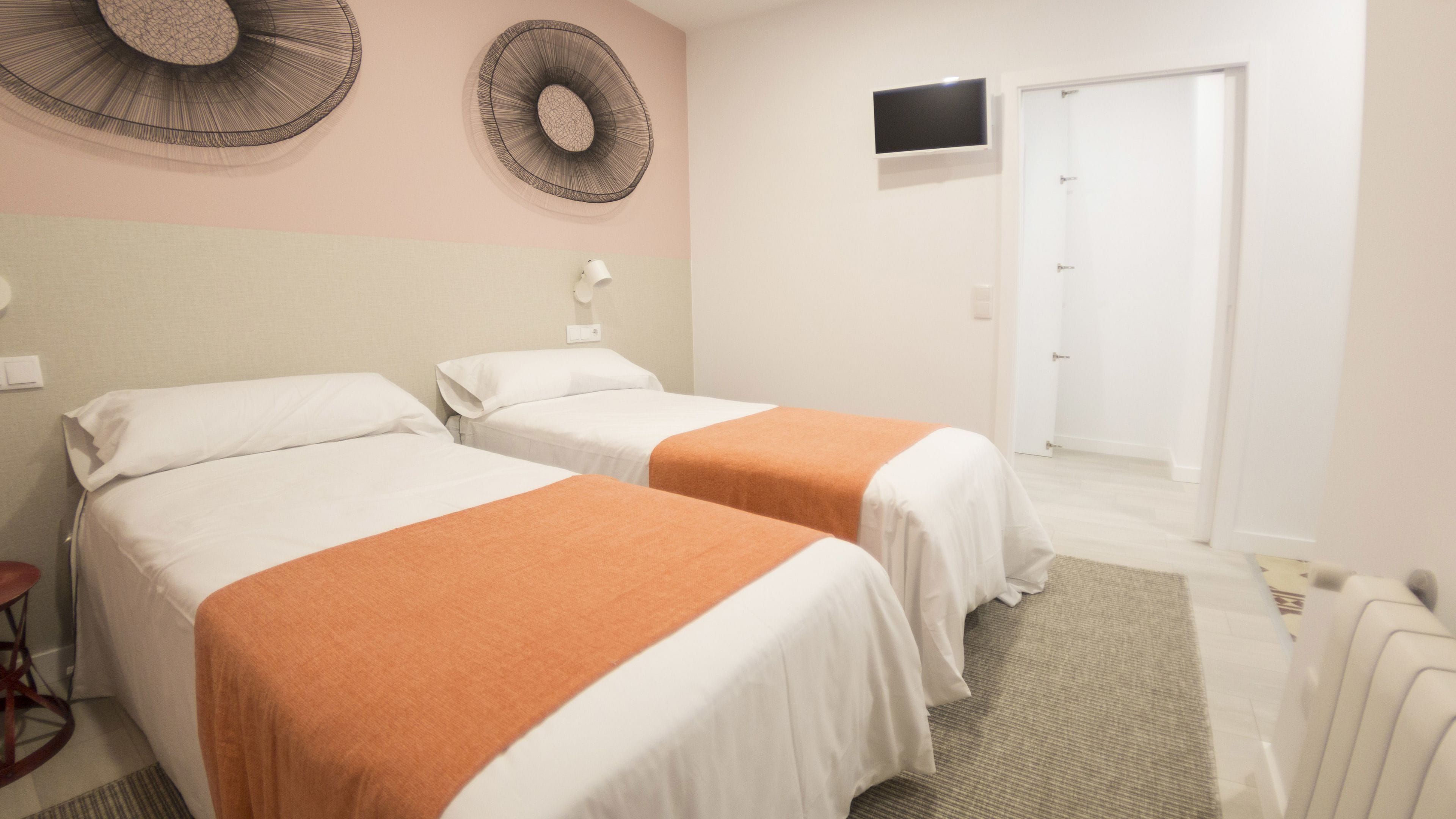 A hotel room with two beds, a television on the wall, and a door.
