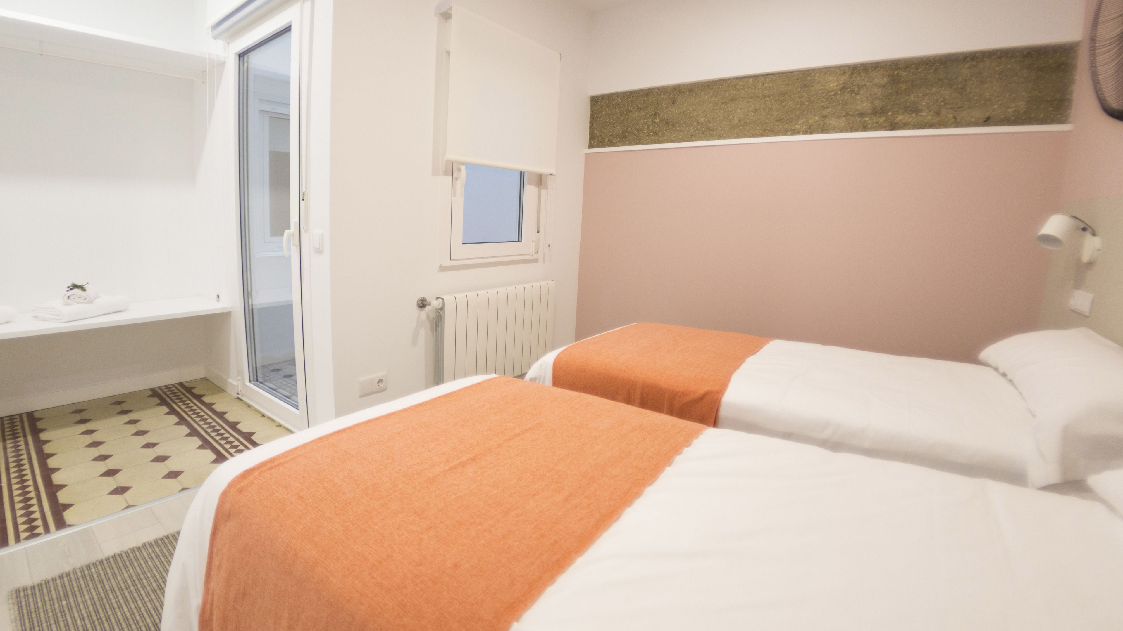 A hotel room with two beds, a shower, a window, and a radiator.