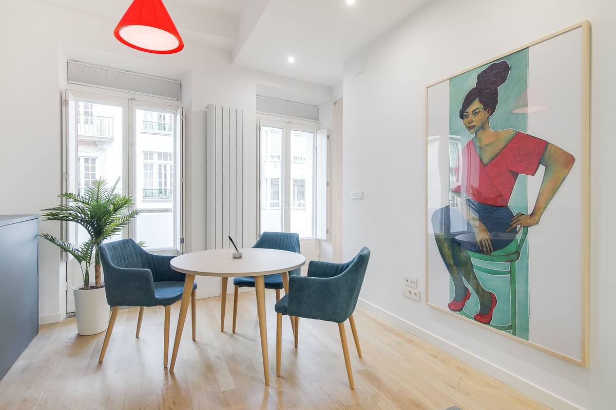 A modern room with a round table, four chairs, a large painting, and a potted plant.