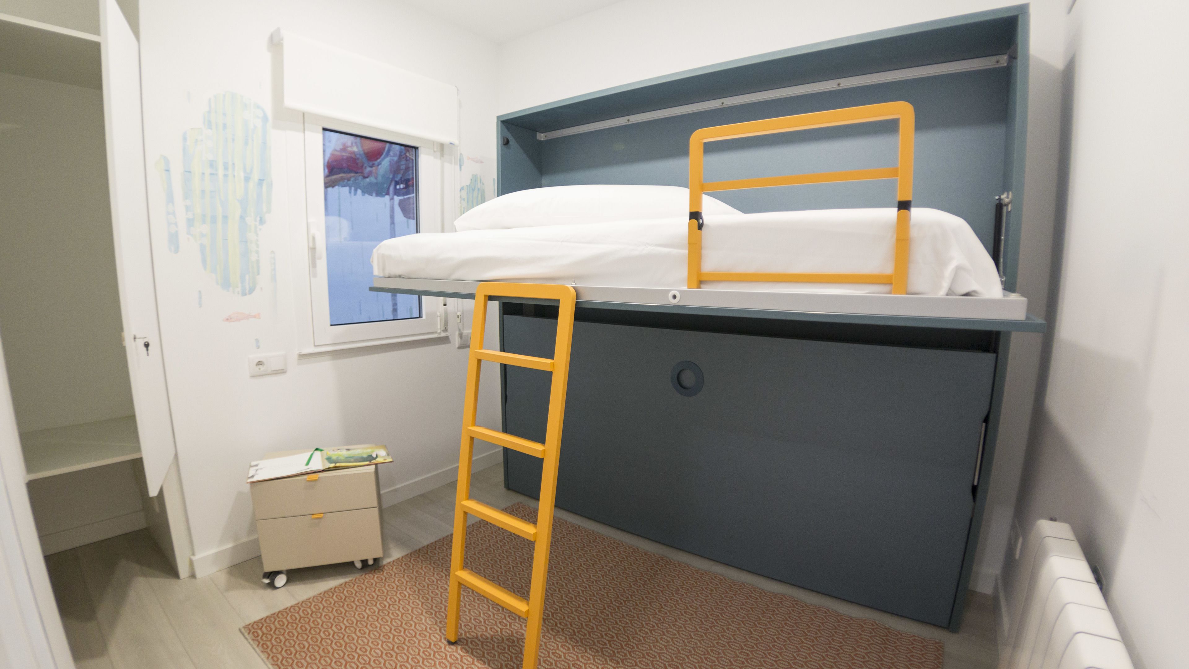 Habitación pequeña con literas, un escritorio y una escalera.
