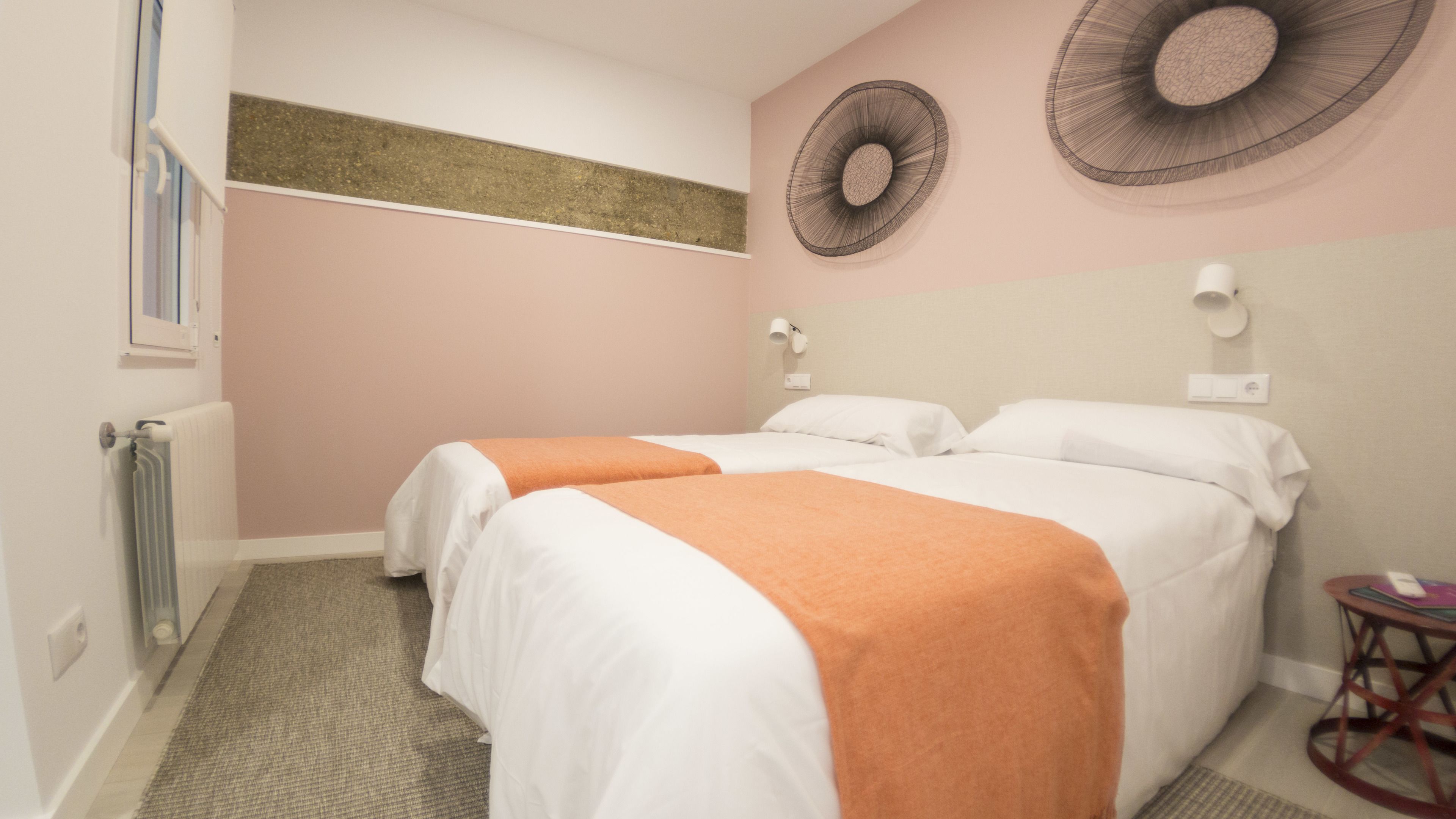 Ein Hotelzimmer mit zwei Betten, einem Heizkörper, einem kleinen runden Tisch und Wandbildern.
