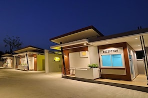 A modern hotel reception area with a reception desk, a sign labeled "RECEPTION," and a small outdoor seating area with plants. - The Rich Resort (Krabi)
