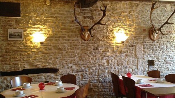 Ein Restaurant mit Steinsäulen und aufgehängten Hirschgeweihen. Die Tische sind mit roten Tischdecken und weißen Tellern gedeckt.