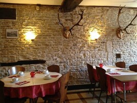 Un restaurante con paredes de piedra y ciervos disecados en las paredes. Las mesas están dispuestas con manteles rojos y platos blancos.