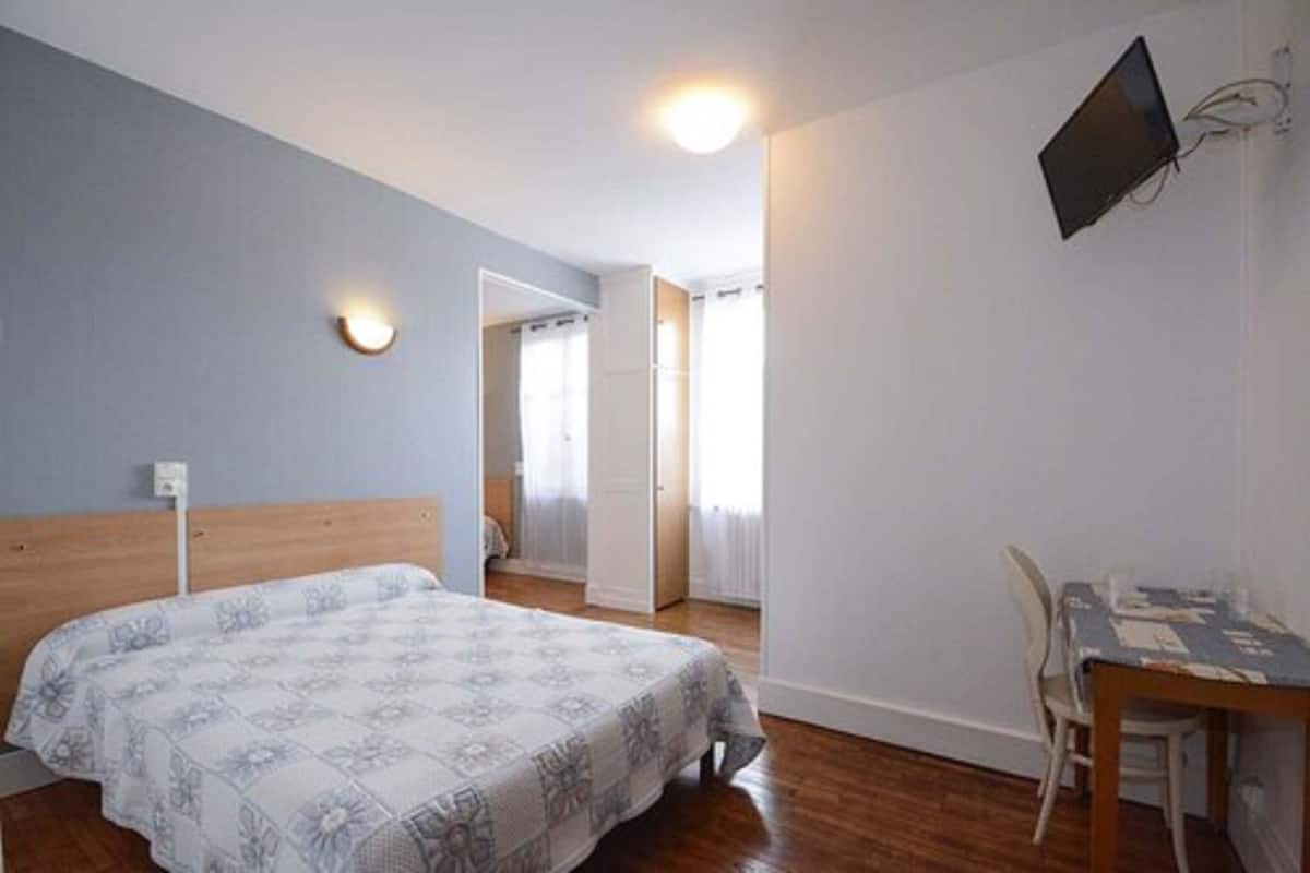 Ein Schlafzimmer mit Bett, Schreibtisch und Stuhl. Ein Fernseher ist an der Wand befestigt.