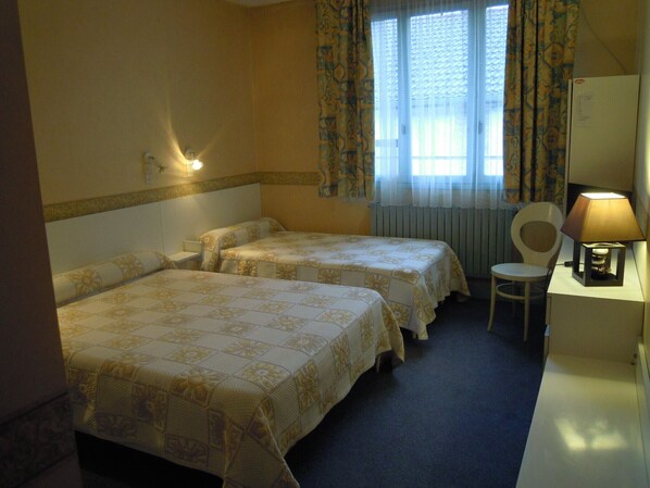 Una habitación de hotel con dos camas, un escritorio con lámpara, una silla y una ventana con cortinas.
