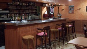 Eine Bar mit Holzwandverkleidung, einer Dartscheibe und einer Auswahl an Flaschen und Gläsern auf Regalen.