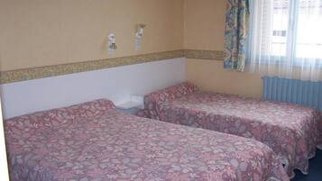 Quarto com duas camas de solteiro, uma mesinha e uma janela com cortinas.