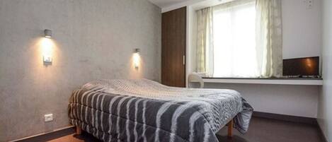 A bedroom with a bed, two wall-mounted lights, a window with curtains, and a TV on a shelf.