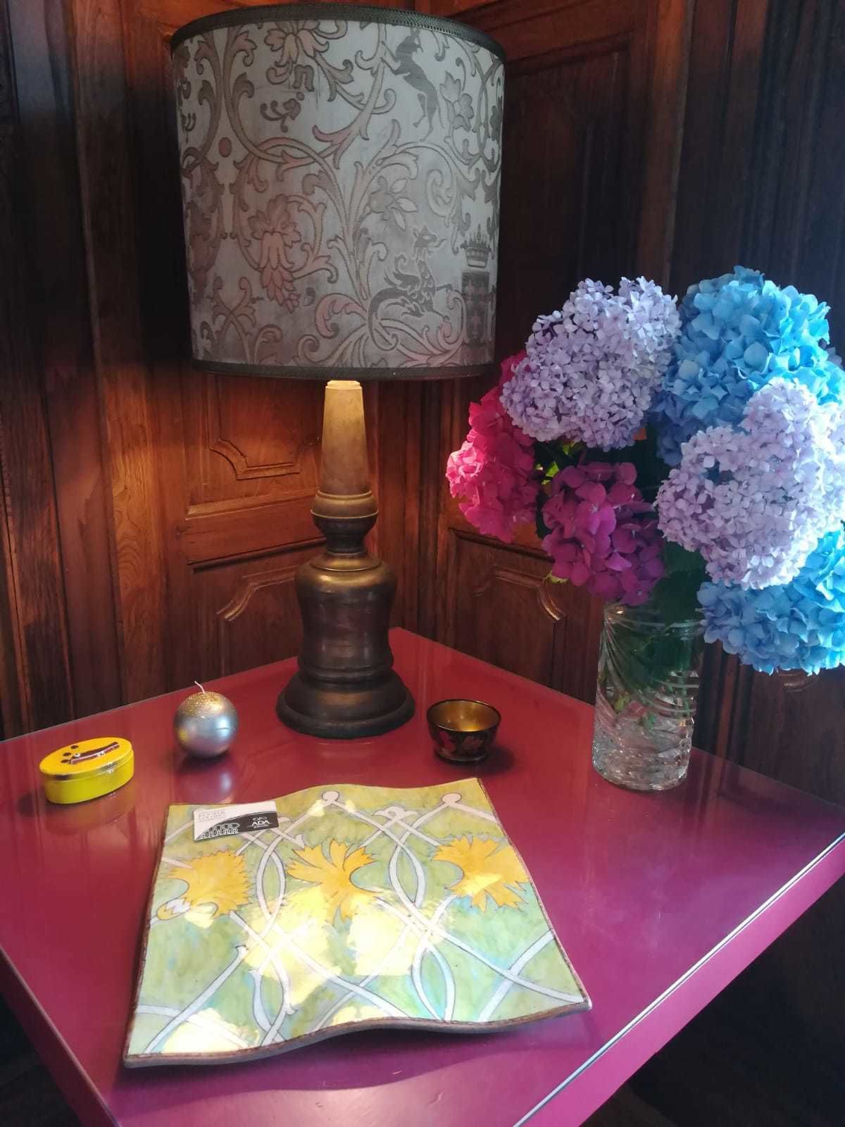 A table with a lamp, a vase of flowers, a small candle, and a decorative box.