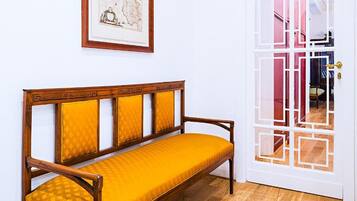 Um banco de madeira com almofadas amarelas em um quarto com piso de madeira e uma porta branca com design geométrico.