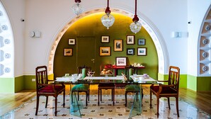 A dining area with a glass table, wooden chairs, and a green wall with framed pictures.