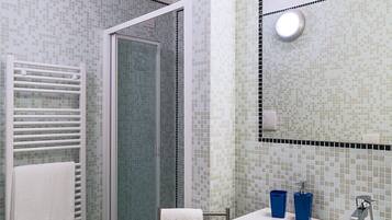 Une salle de bain équipée d’une douche, de toilettes, d’un lavabo et d’un miroir, les murs étant recouverts de carreaux de mosaïque.