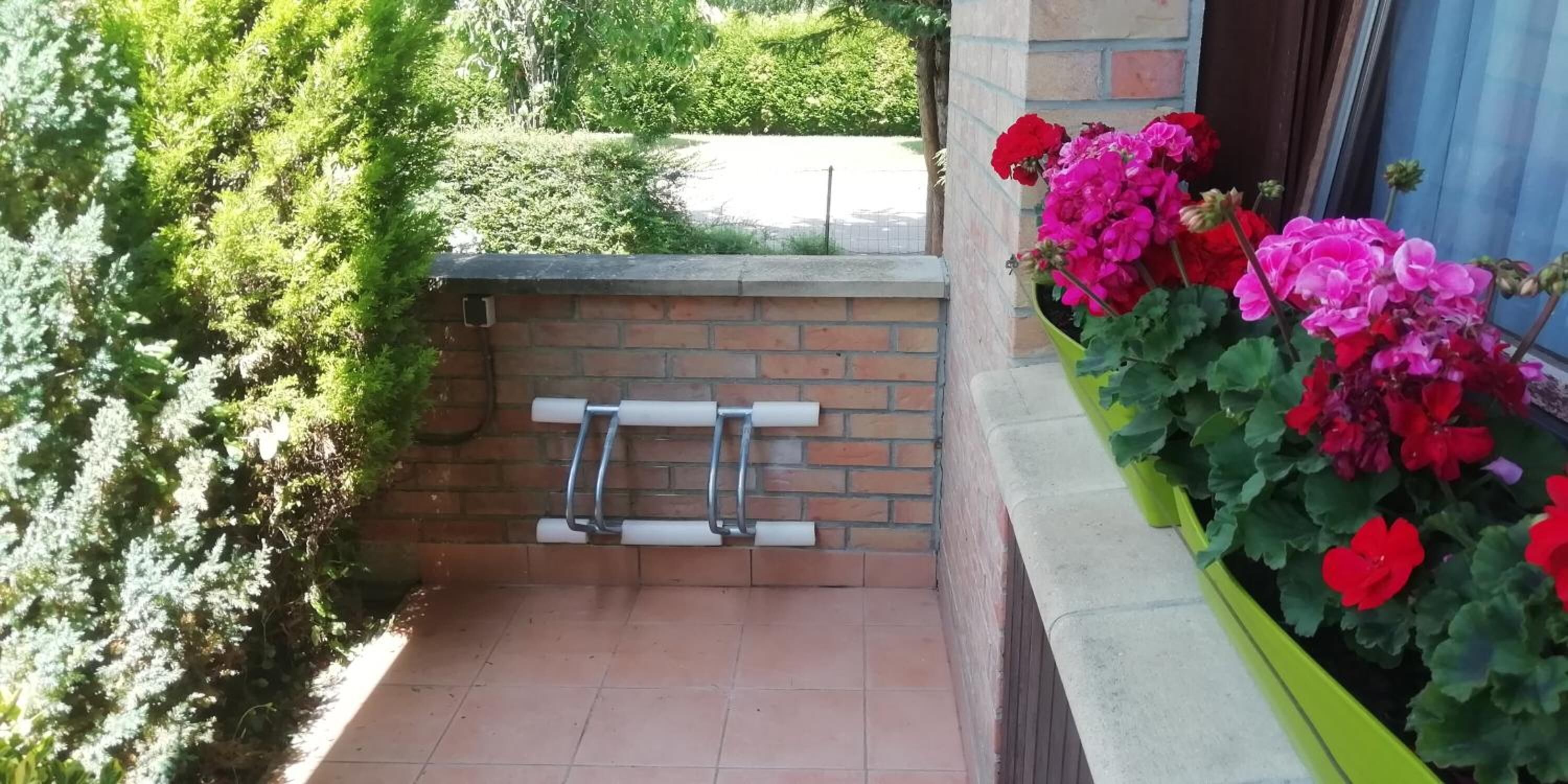 A small outdoor area with a brick wall, a metal bench, and a planter with red and pink flowers.