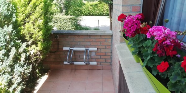 Un pequeño espacio al aire libre con un muro de ladrillo, un banco de metal y una jardinera con flores rojas y rosas.