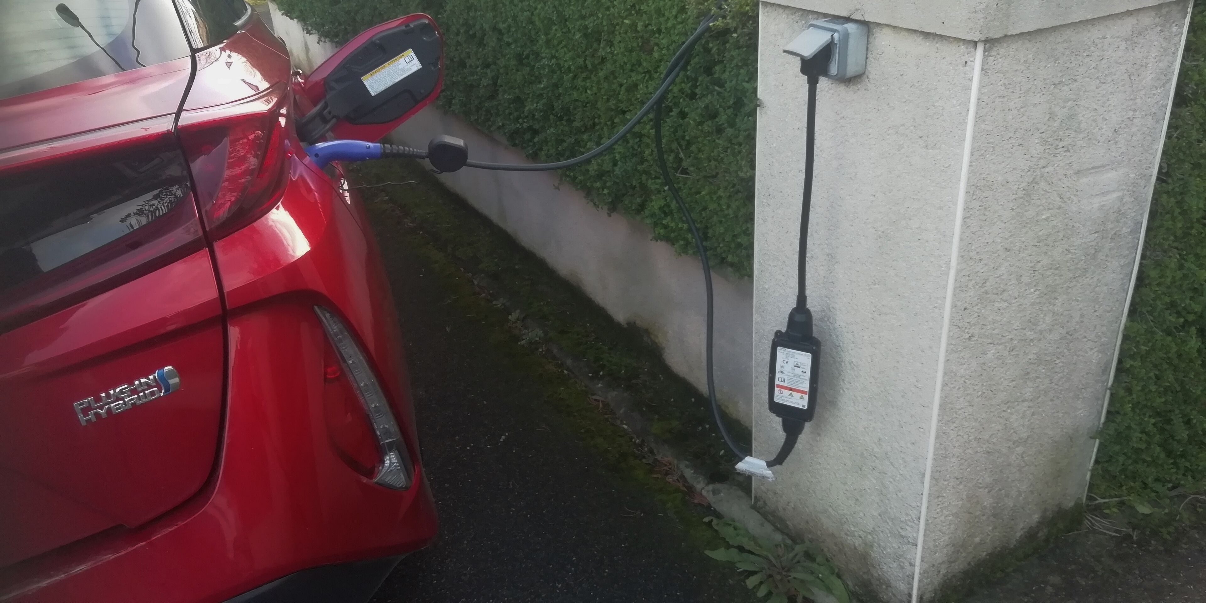 Ein rotes Hybridauto, das neben einer Ladestation geparkt ist.