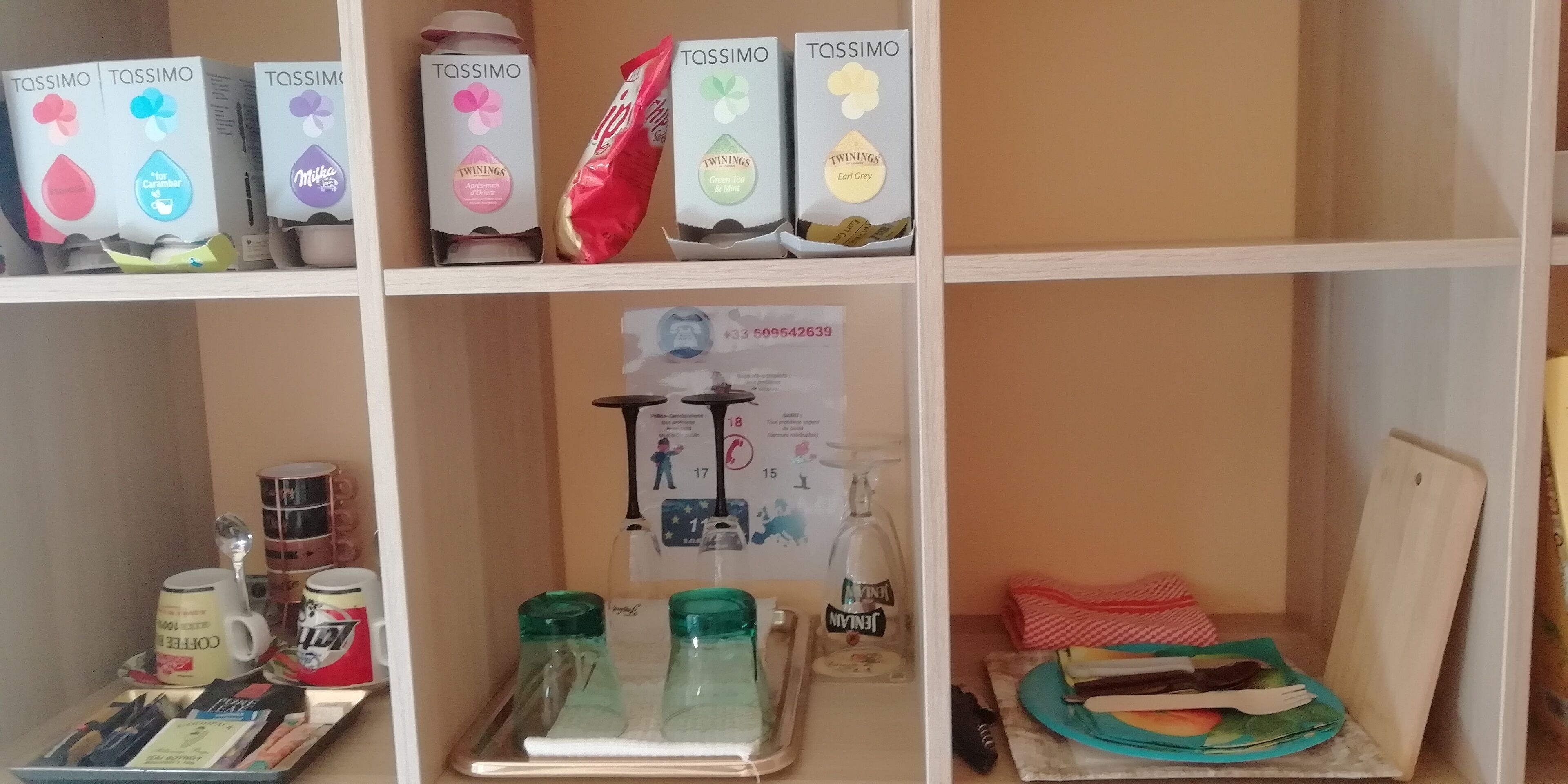 Een plank met Tassimo-cups, een koffieapparaat en een poster.