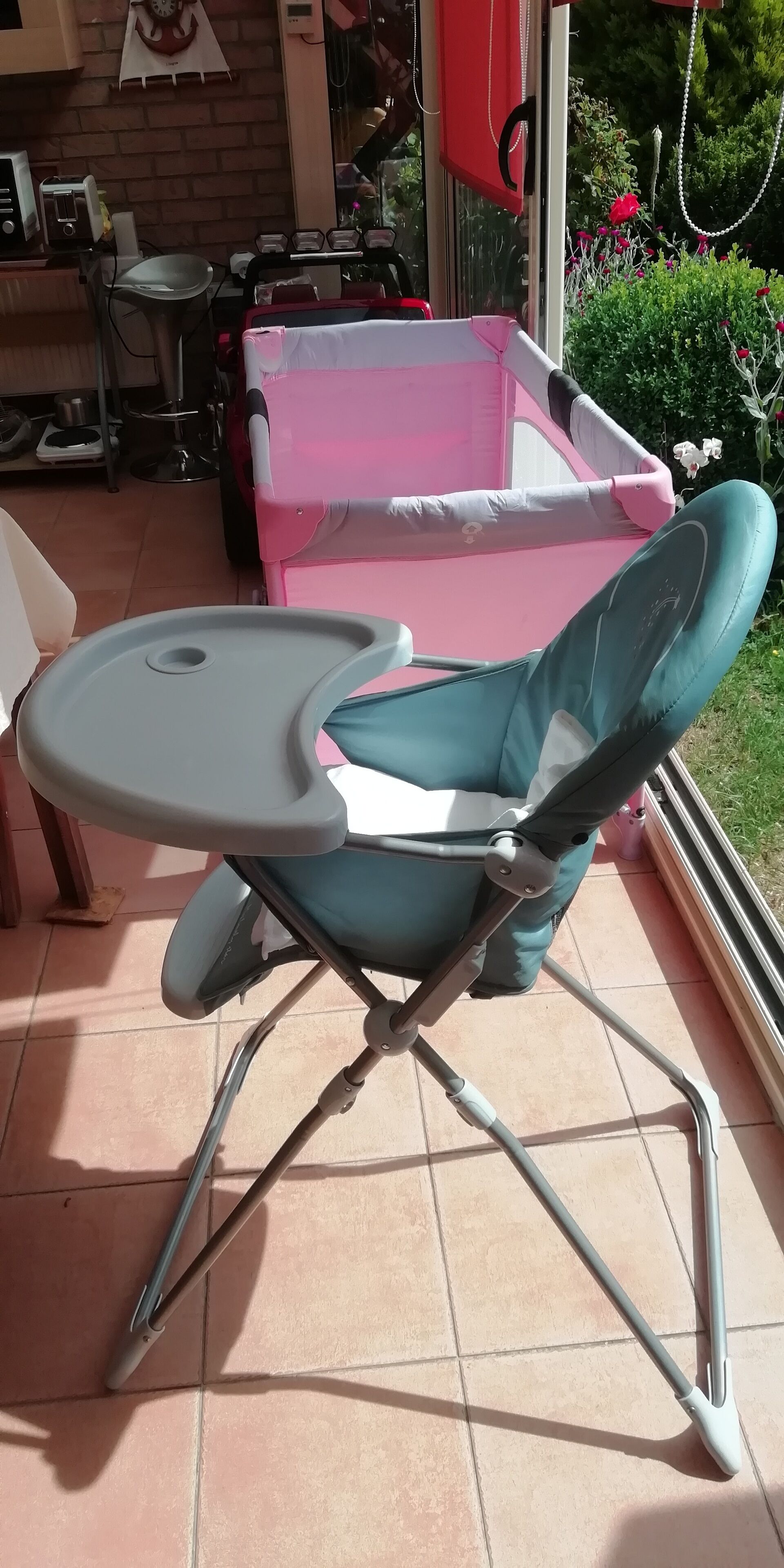 Una silla plegable con una mesita, ubicada en un patio con baldosas y vistas a un jardín y un muro de ladrillo.