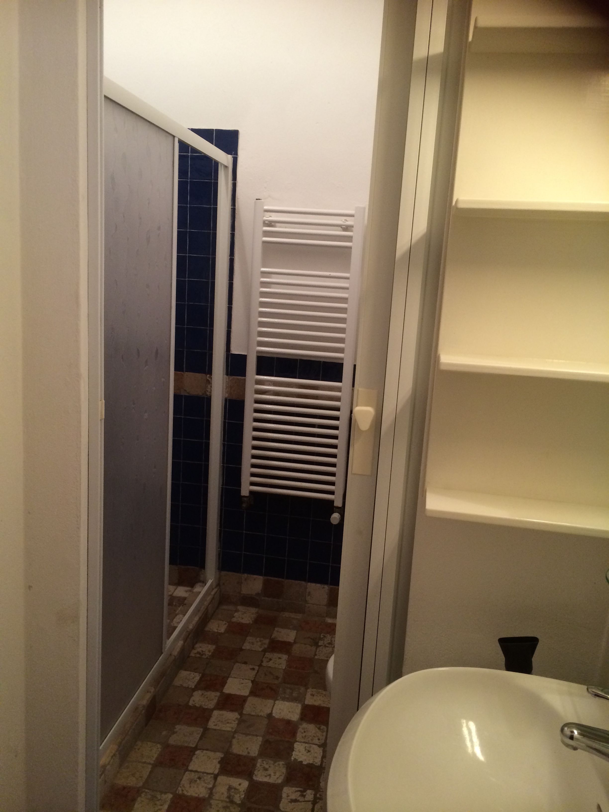 A bathroom with a white sink, a shower with a white door, and a tiled floor.