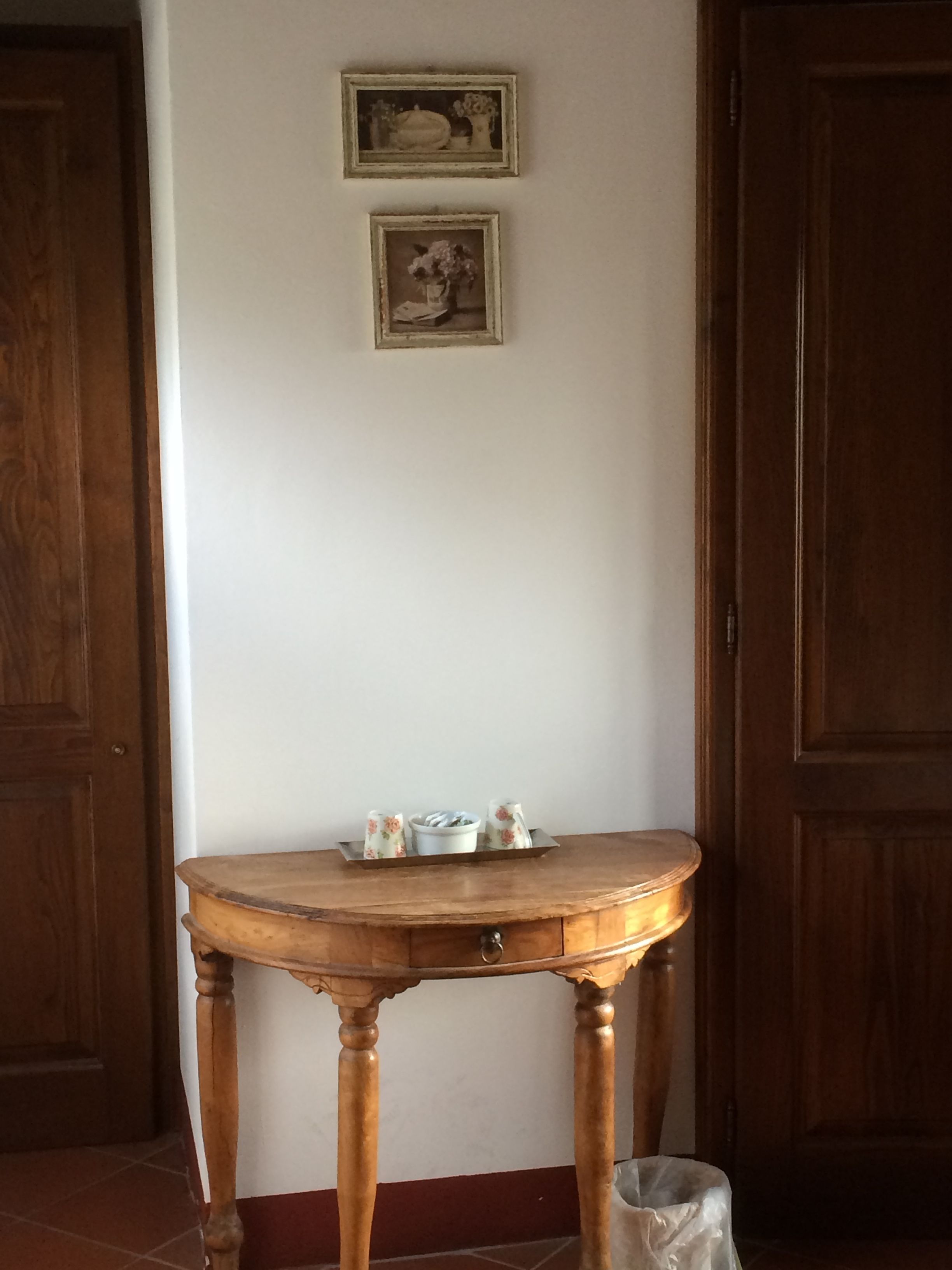 Ein Holztisch mit einer Auflage voller Gegenstände vor einer weißen Wand, begrenzt von zwei Holztüren.
