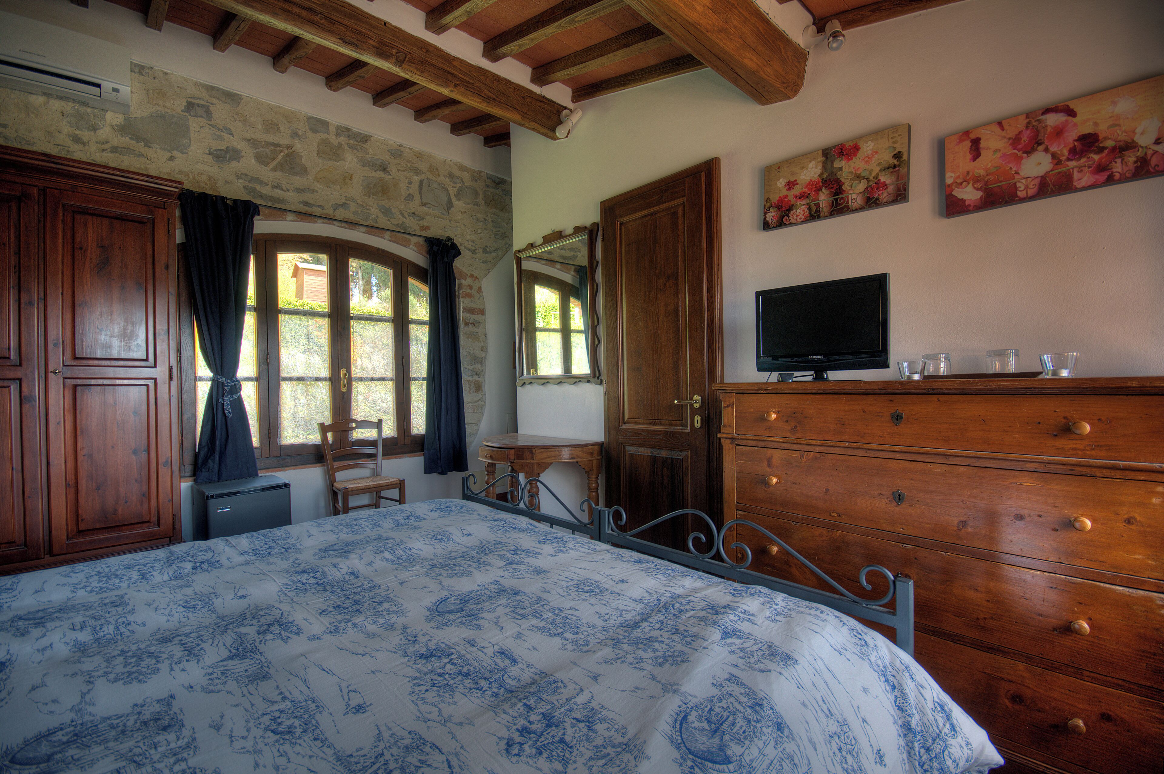 Una camera da letto con un letto, una cassettiera in legno, TV e parete in pietra.