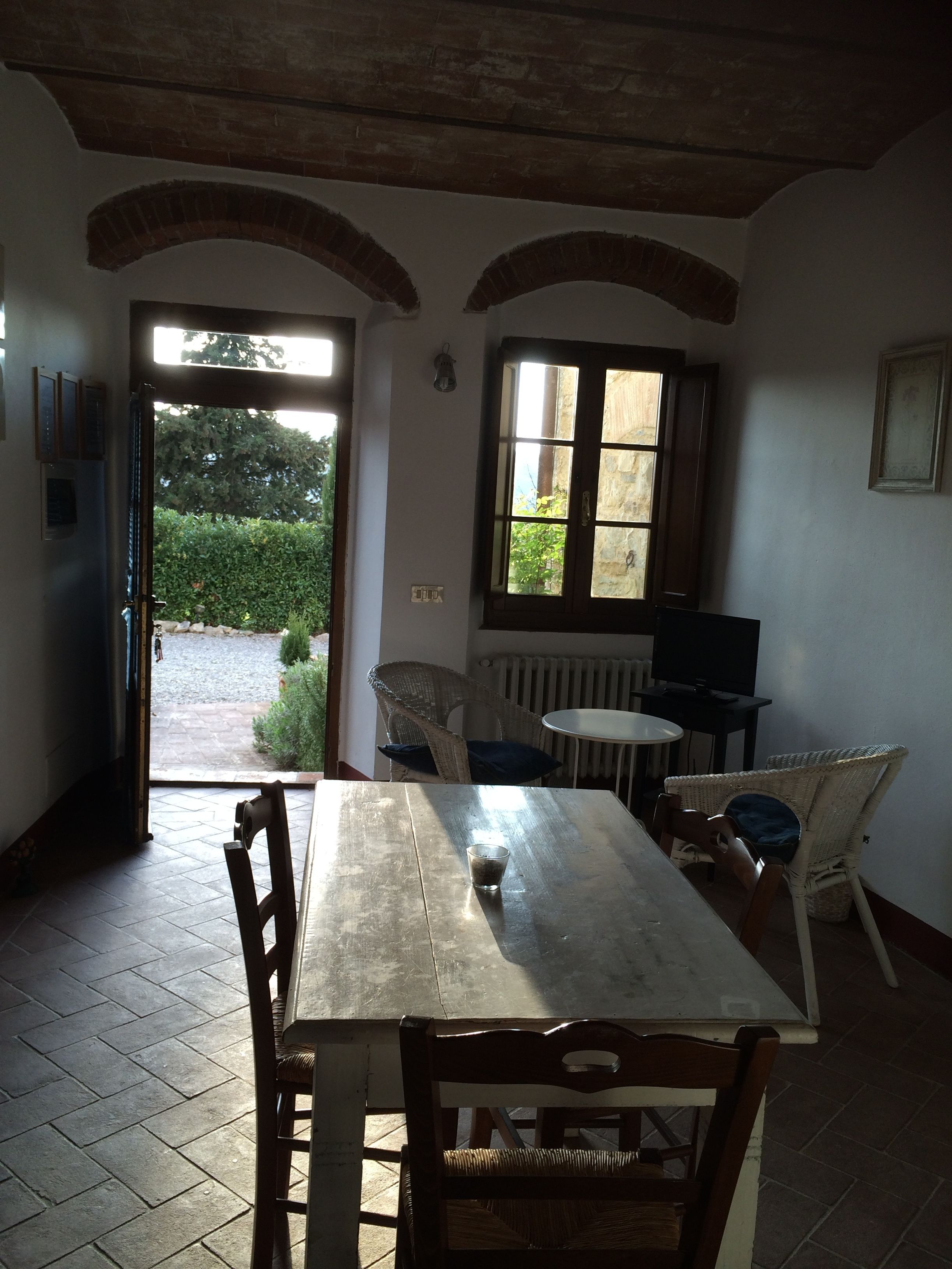A dining area with a wooden table and chairs, a window with a view of greenery, and a radiator on the wall.