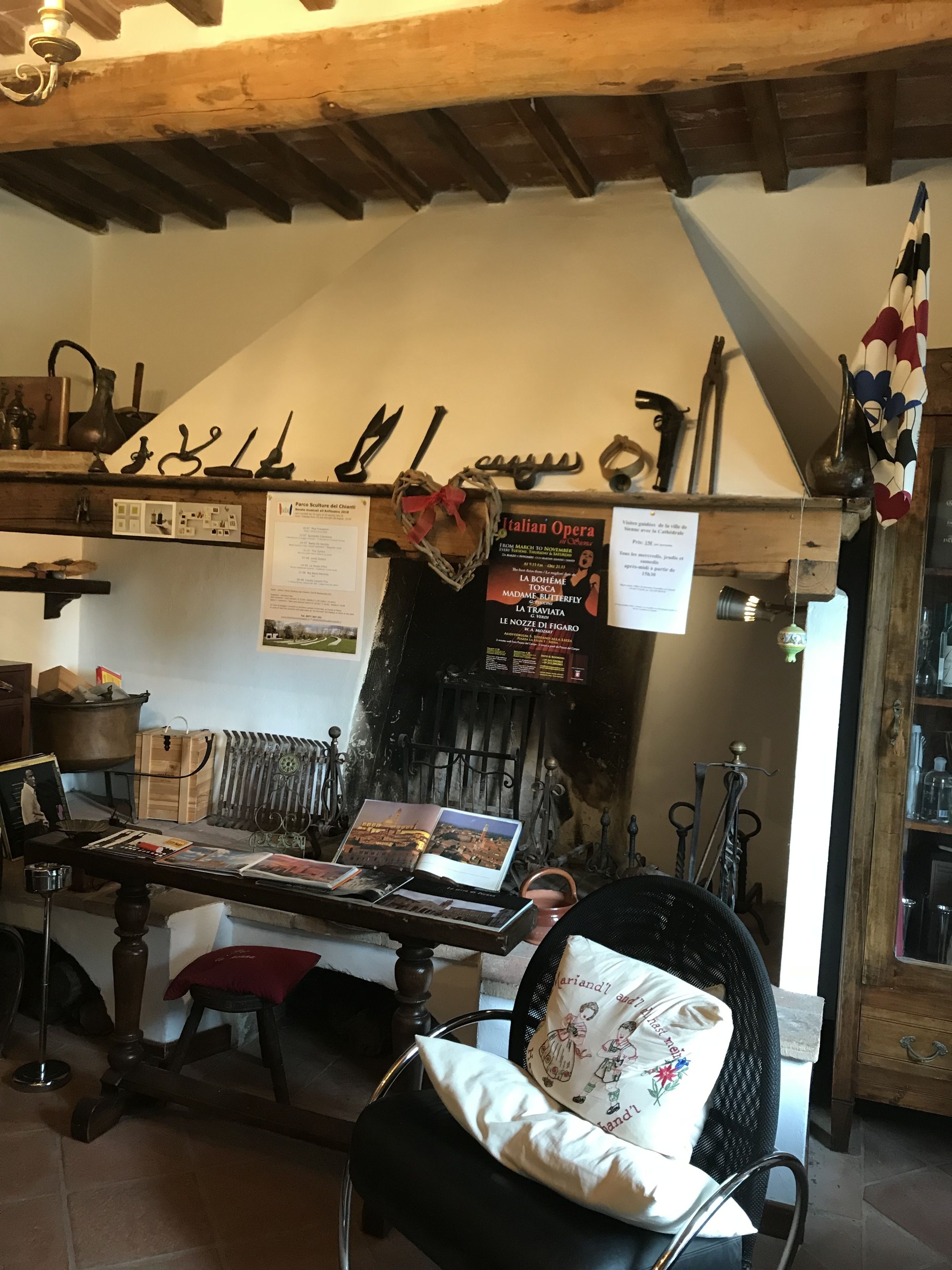 Un intérieur rustique avec des poutres apparentes, une cheminée et divers objets historiques exposés sur des étagères.