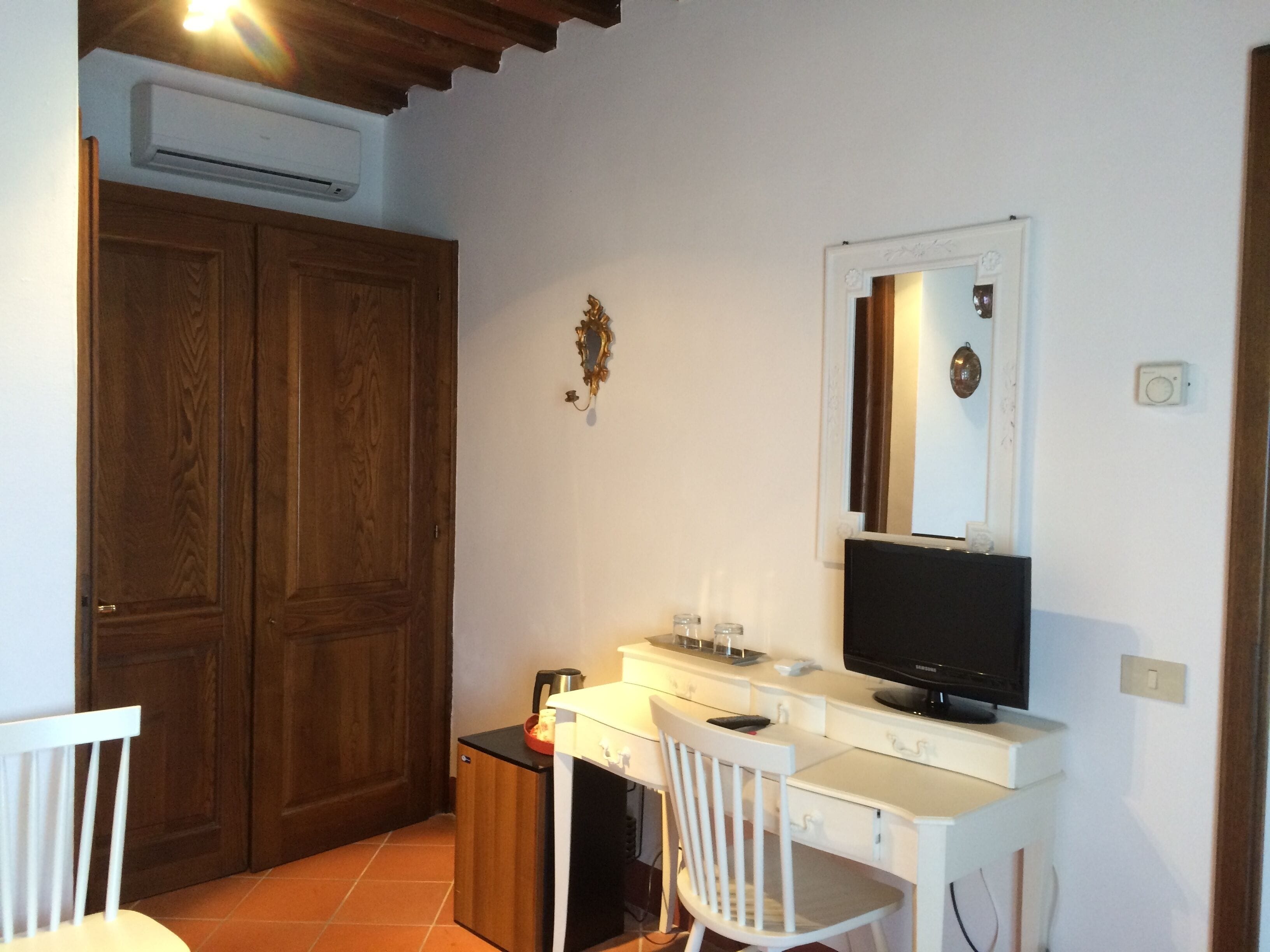 Una habitación pequeña con un armario de madera, un escritorio con computadora, una silla y un espejo en la pared.