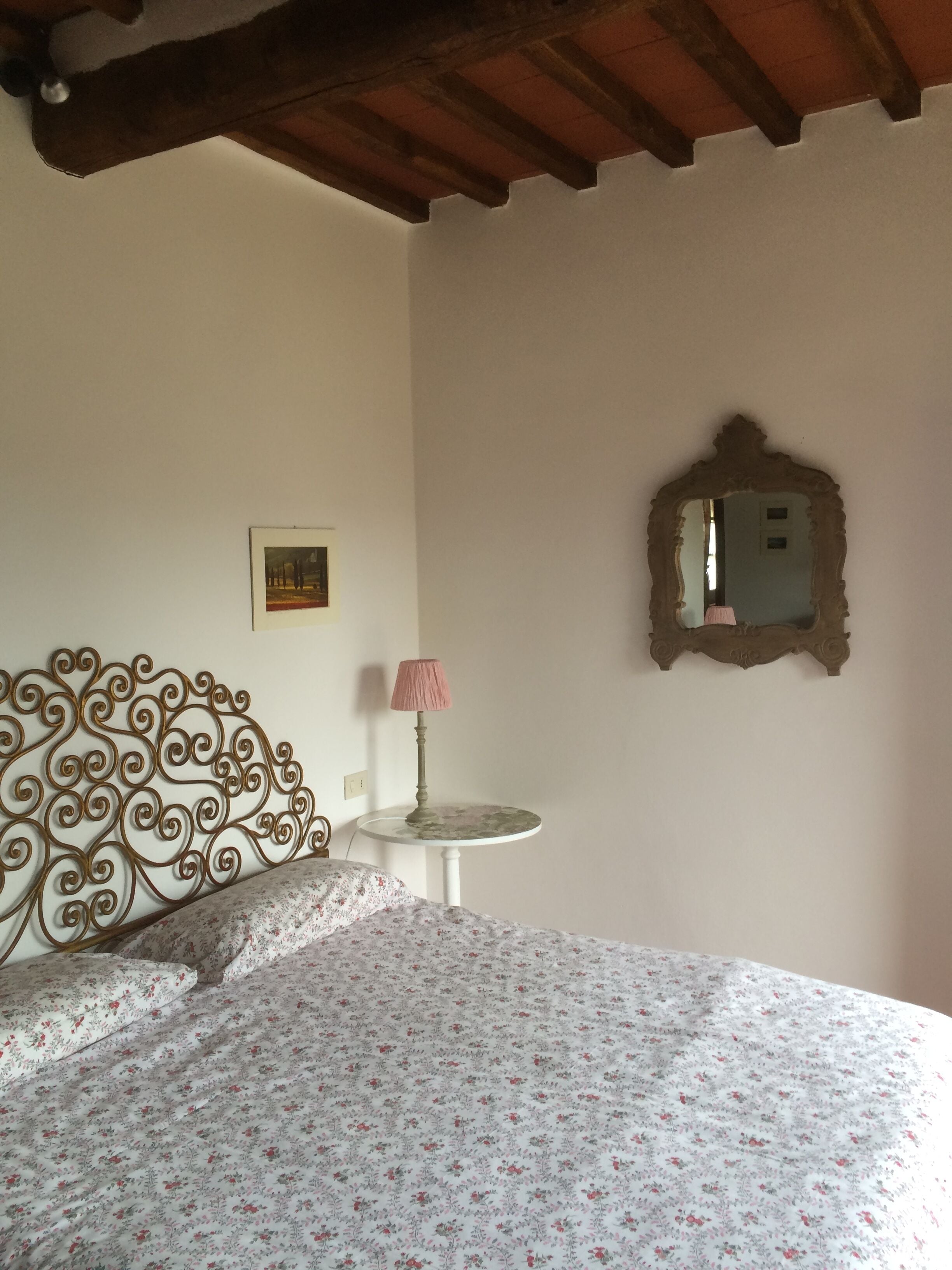 Ein Schlafzimmer mit einem Bett, einem kleinen Tisch mit Lampe, einem Spiegel und einem Bild an der Wand.