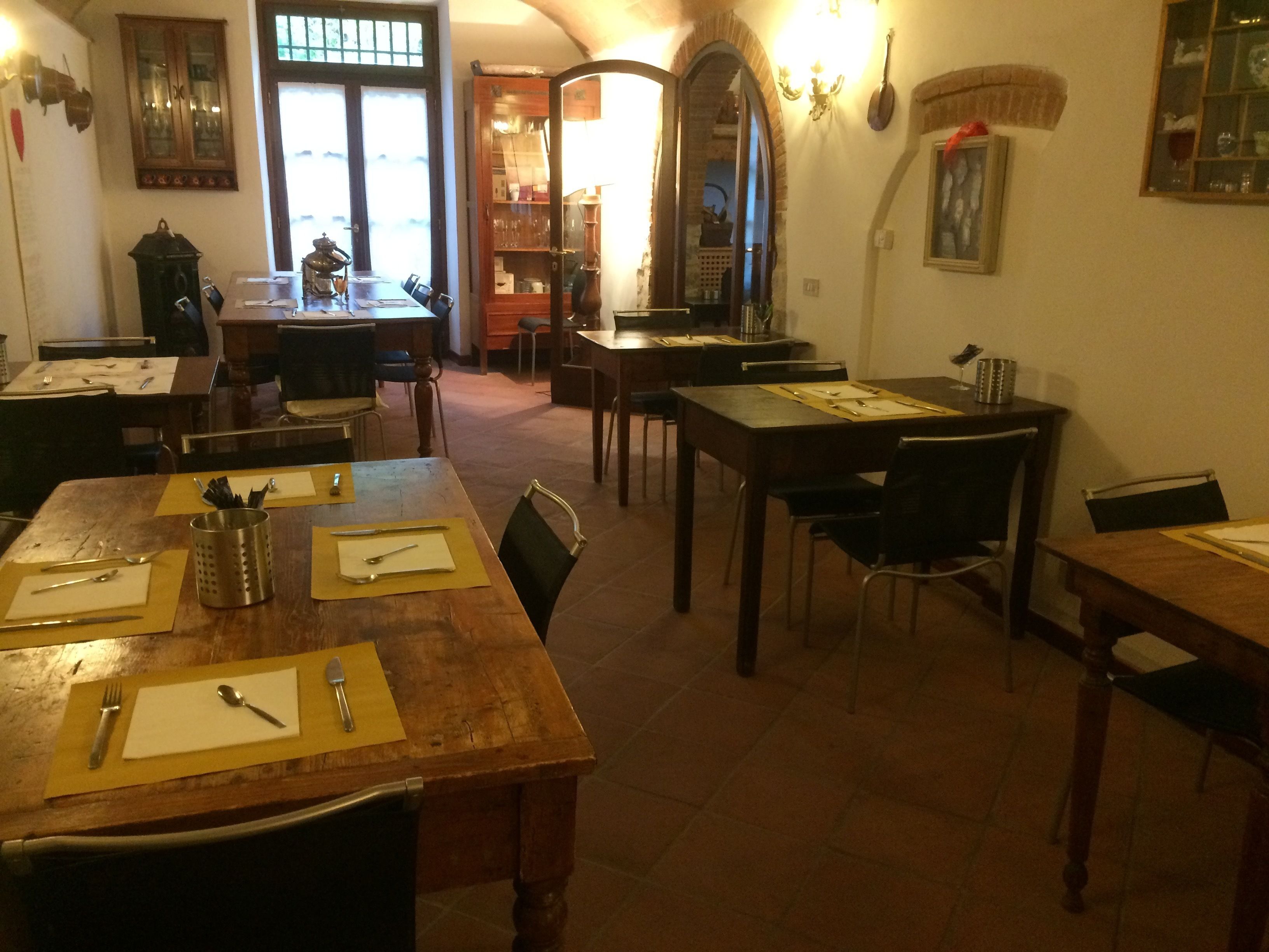 Uma sala de jantar com mesas e cadeiras de madeira, uma cozinha ao fundo e um espelho grande na parede.