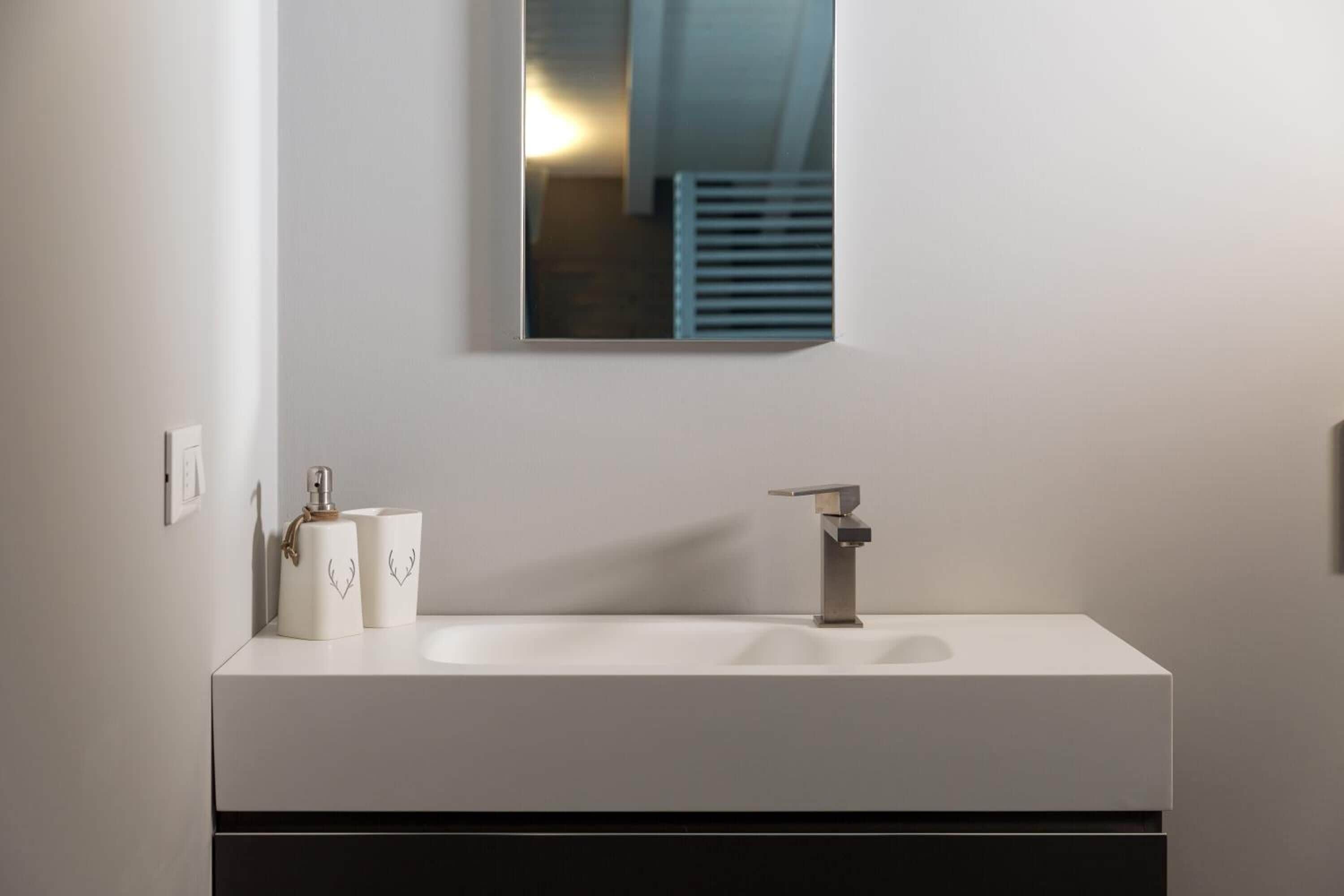 A modern bathroom with a white sink, a mirror, and two toiletry bottles.