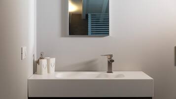 A modern bathroom with a white sink, a mirror, and two toiletry bottles.
