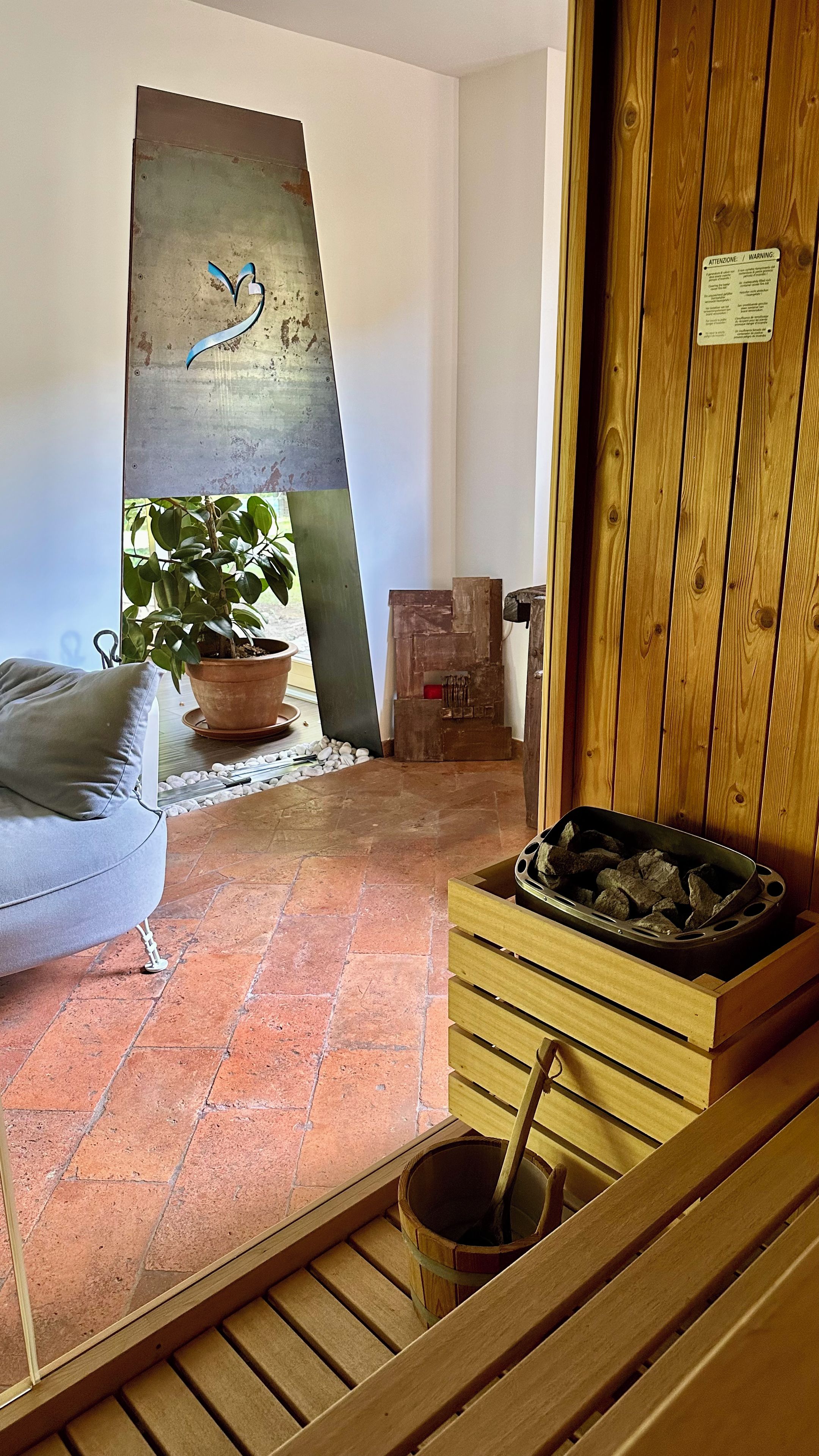 A room with a wooden bench, a potted plant, a metal sculpture, and a fireplace.
