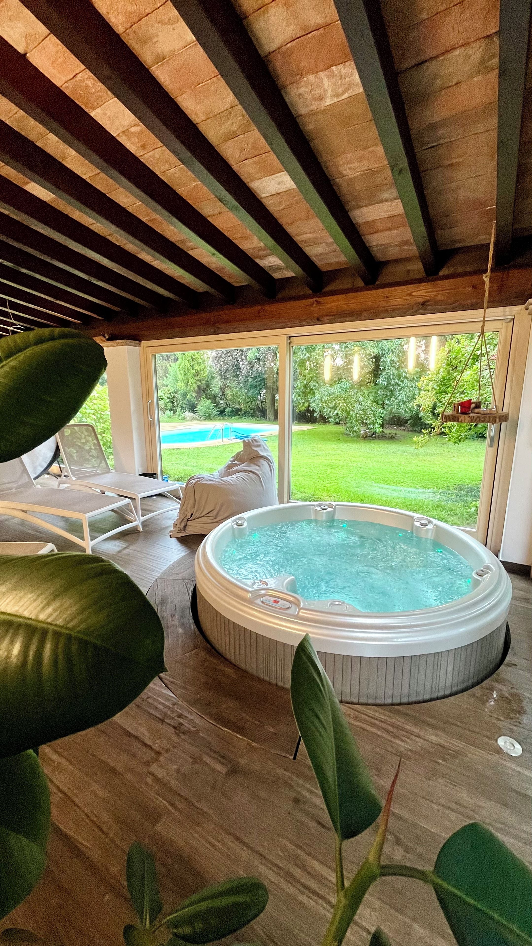 Un jacuzzi en un área exterior cubierta con vistas a una piscina y follaje.