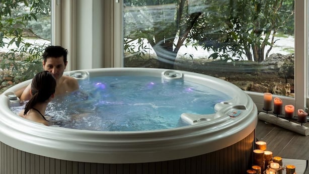 Un jacuzzi con dos personas adentro, rodeado de velas y vistas al verdor exterior.