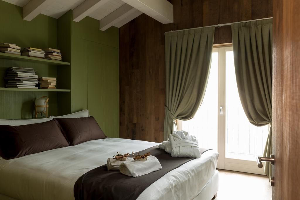 Una cama bien tendida con una colcha blanca y marrón, un conjunto de libros en una estantería y una ventana con cortinas.