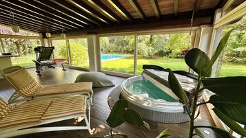 A sunlit room with a pool, lounge chairs, and a hot tub.