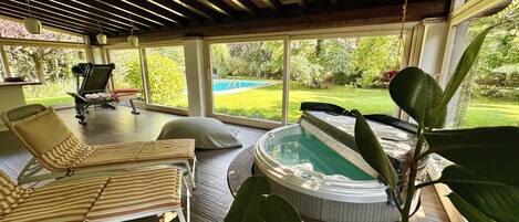 Ein sonnendurchfluteter Raum mit Pool, Liegestühlen und Whirlpool.