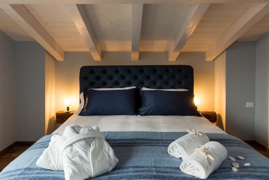 A bedroom with a tufted headboard, two bedside lamps, a bed with a striped blue and white bedspread, and two rolled towels on the bed.