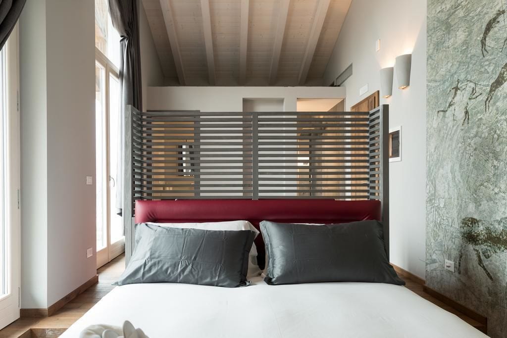 Un dormitorio moderno con cama, cabecero rojo y una ventana grande.