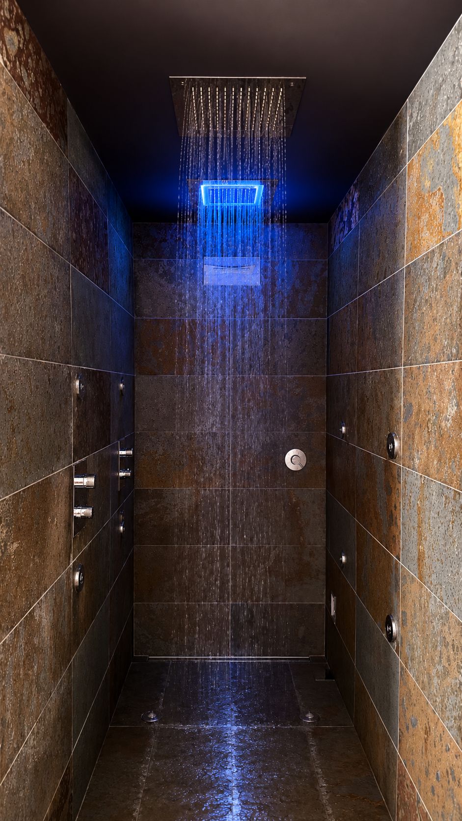 Une douche moderne dotée d’un élément décoratif vertical en eau et d’un panneau de commande mural.