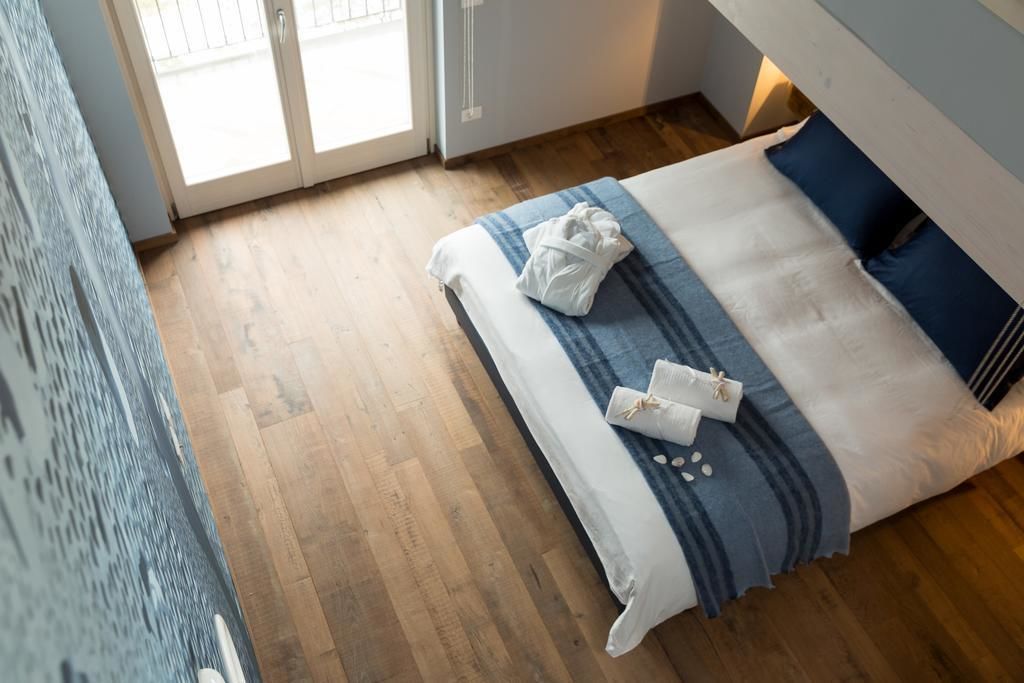A bedroom with a wooden floor, a bed with a blue and white striped blanket, and a white towel on the bed.