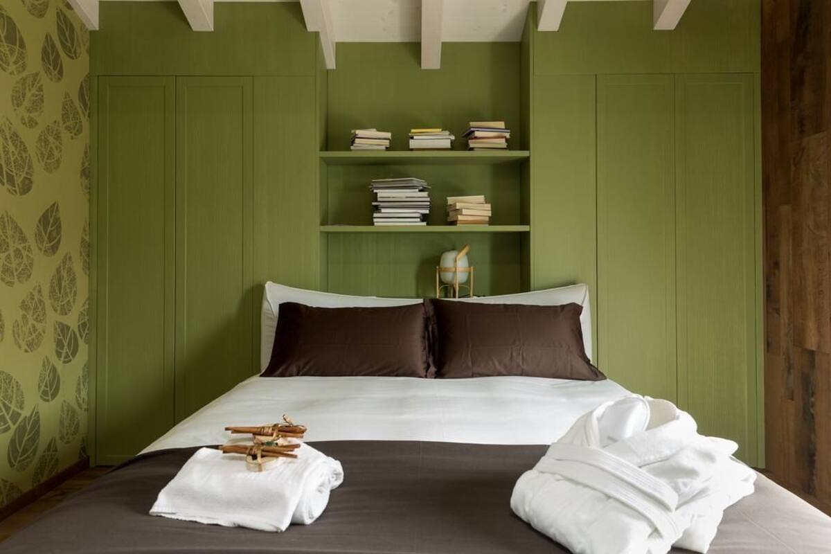 A neatly made bed with white linens, a dark brown headboard, and a wooden nightstand with a lamp.