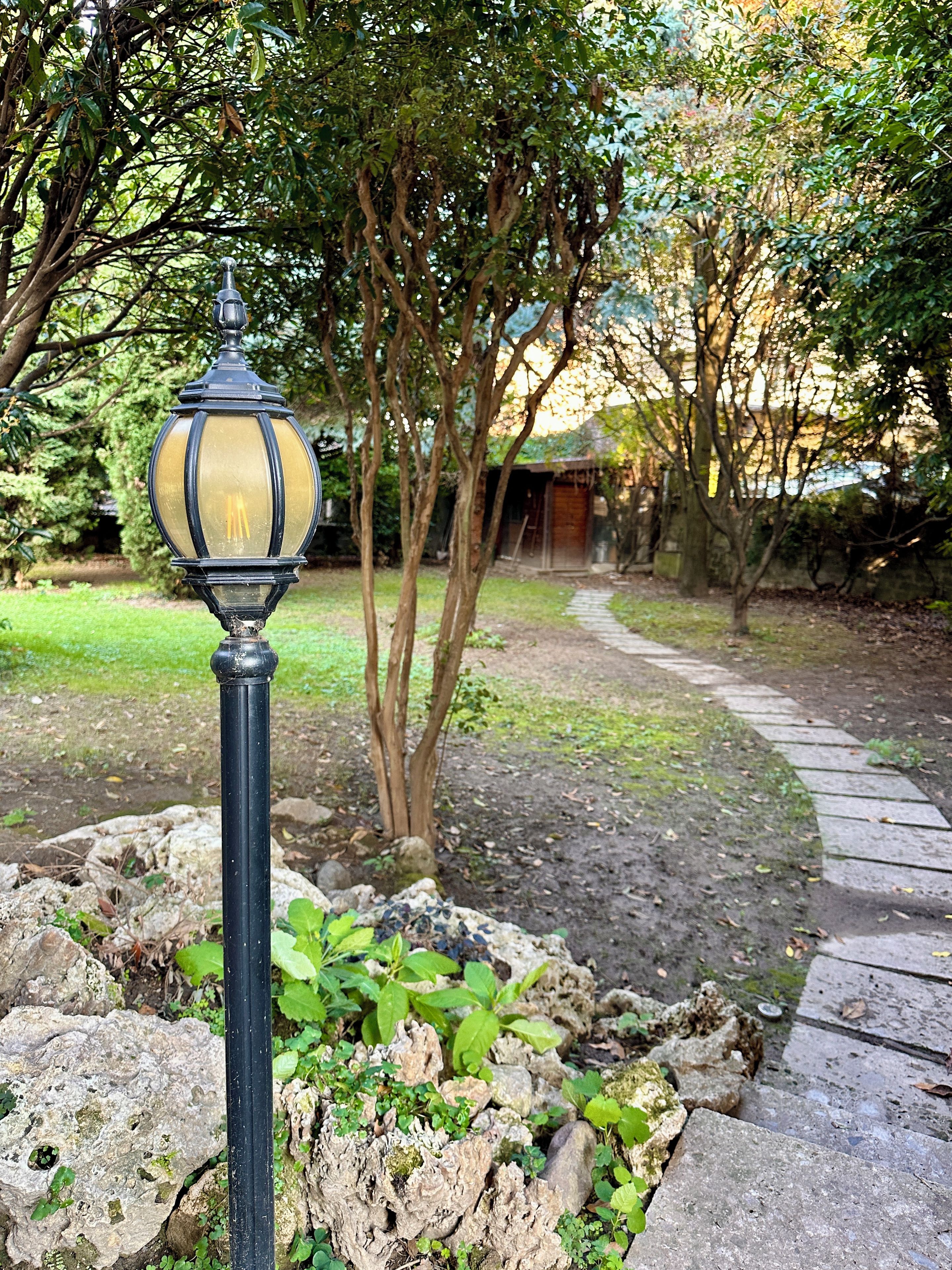 A garden with a pathway, a lamp post, and trees.
