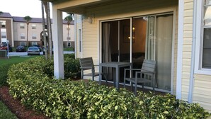 Un espace extérieur abrité, aménagé avec une table et des chaises, et entouré d’arbustes bien entretenus.