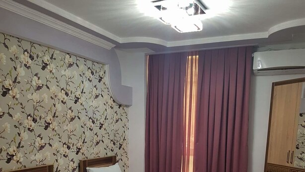 A hotel room with two beds, a wooden wardrobe, a small table, and a floral wallpaper. - Georgian Palace (Kutaisi)